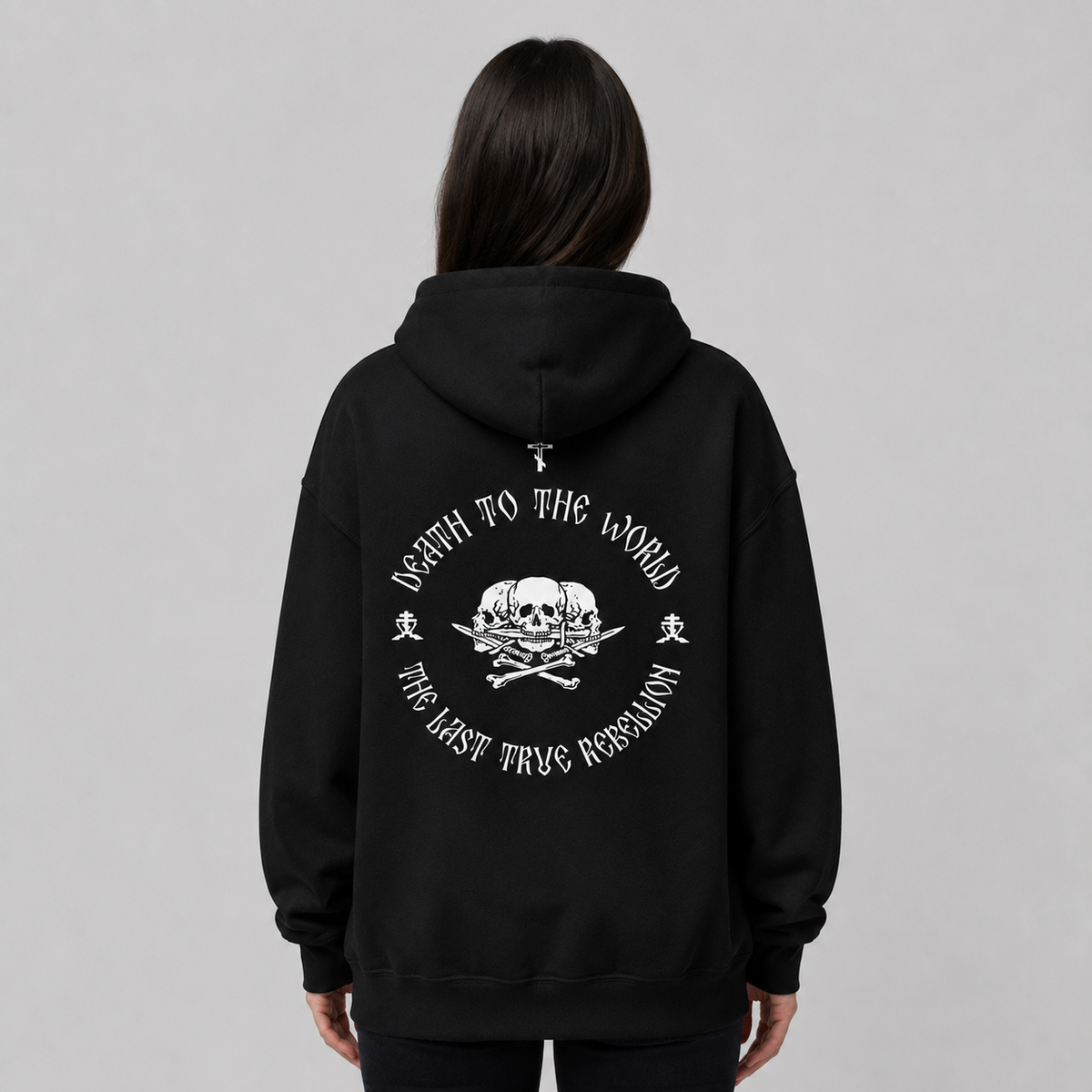 Rückansicht einer Person in schwarzem Pullover-Hoodie mit großem weißem Rückendruck. Das Design zeigt einen Totenkopf mit gekreuzten Knochen inmitten der kreisförmigen Aufschrift „THE LAST TRUE REBELLION“.
