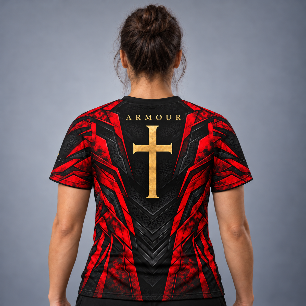 A woman viewed from the back wearing a short-sleeve athletic jersey with a red and black geometric design, a large gold cross on the back, and the word ARMOUR above it, against a plain gray studio background.