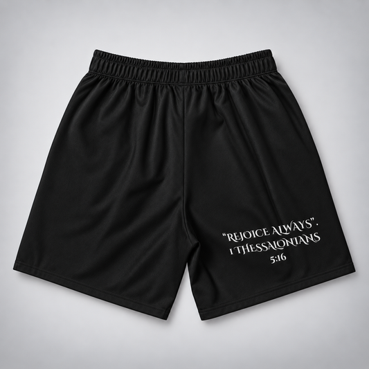 Black athletic shorts with an elastic waistband and white printed text reading “REJOICE ALWAYS. I THESSALONIANS 5:16” on the lower right leg, shown flat against a light gray background.