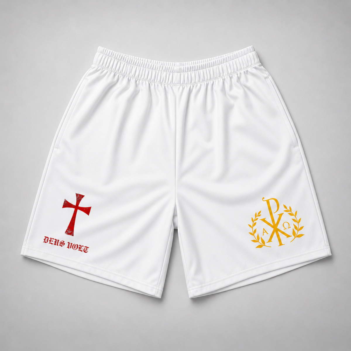 White athletic shorts with an elastic waistband, featuring a red cross and 'DEUS VULT' text on the left leg, and a gold Chi-Rho emblem with laurel leaves on the right leg, displayed flat on a gray background.