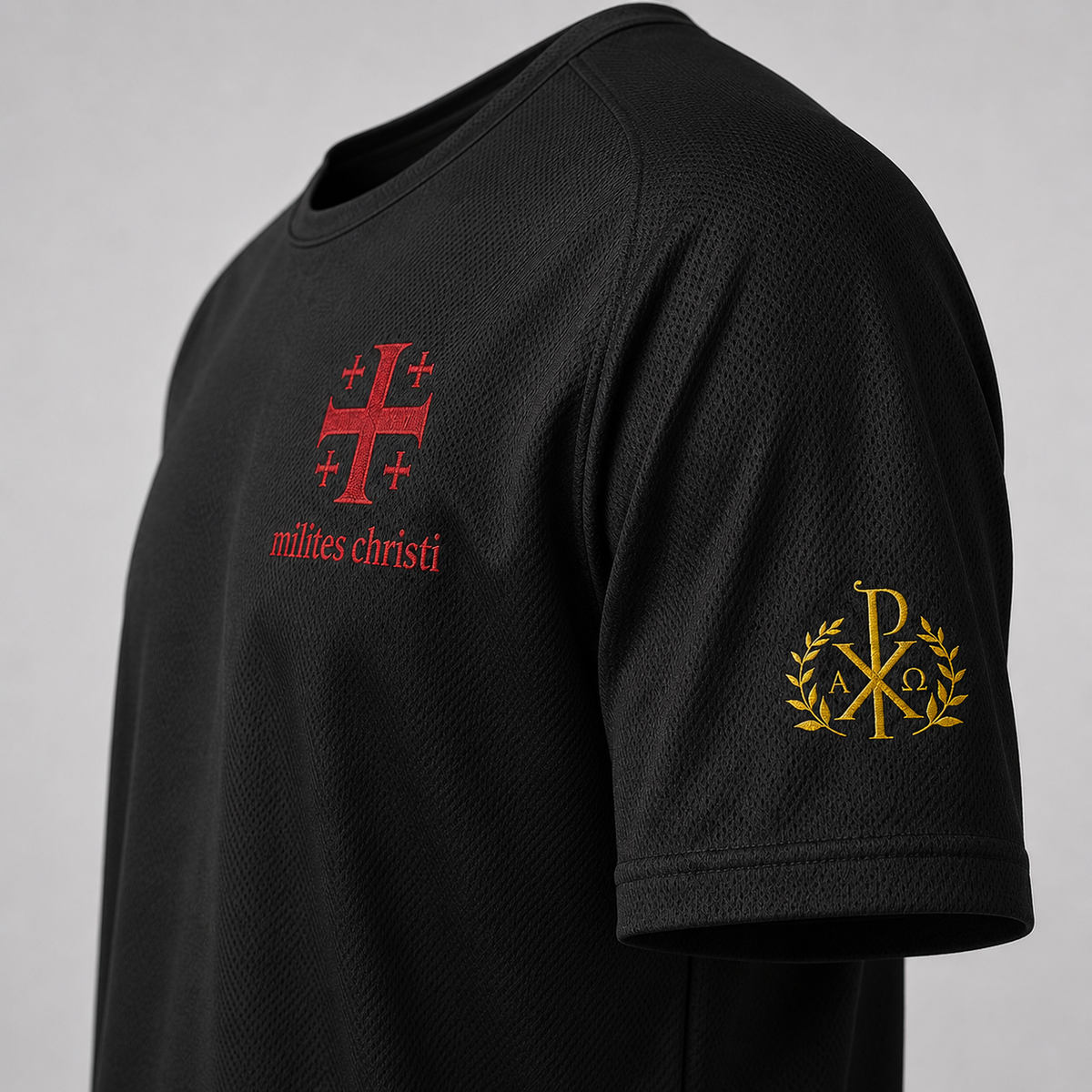 Close-up of a black short-sleeve athletic t-shirt featuring a red 'milites christi' cross logo on the chest and a gold monogram logo on the sleeve, set against a neutral gray background.