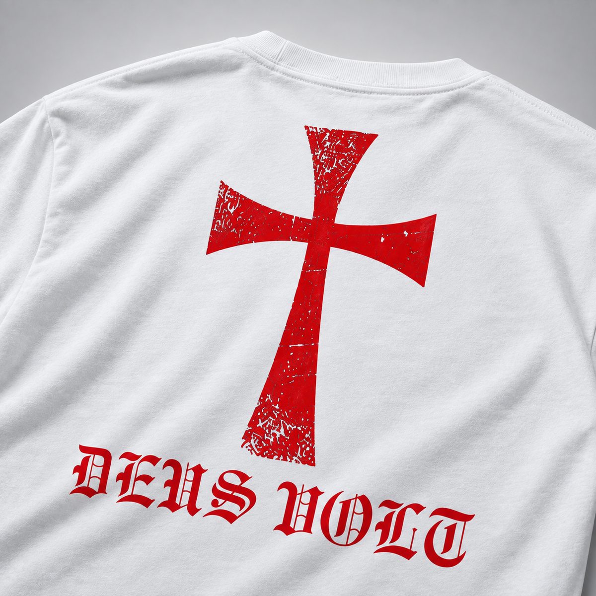 Rückansicht eines weißen T-Shirts mit großem rotem Kreuzmotiv im Used-Look und roter gotischer Aufschrift „DEUS VOLT“ darunter vor neutralem grauem Hintergrund.