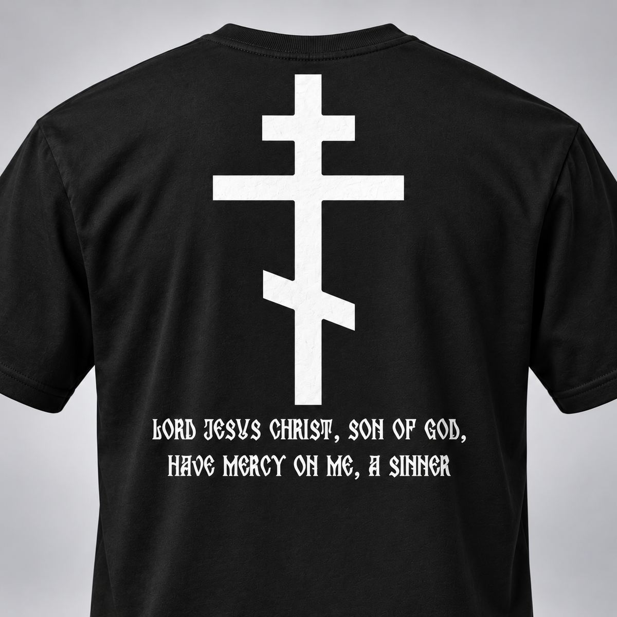 Rückansicht eines schwarzen kurzärmeligen T-Shirts mit großem weißem ostorthodoxem Kreuzmotiv und der weißen gotischen Aufschrift „Herr Jesus Christus, Sohn Gottes, erbarme Dich meiner, des Sünders“.