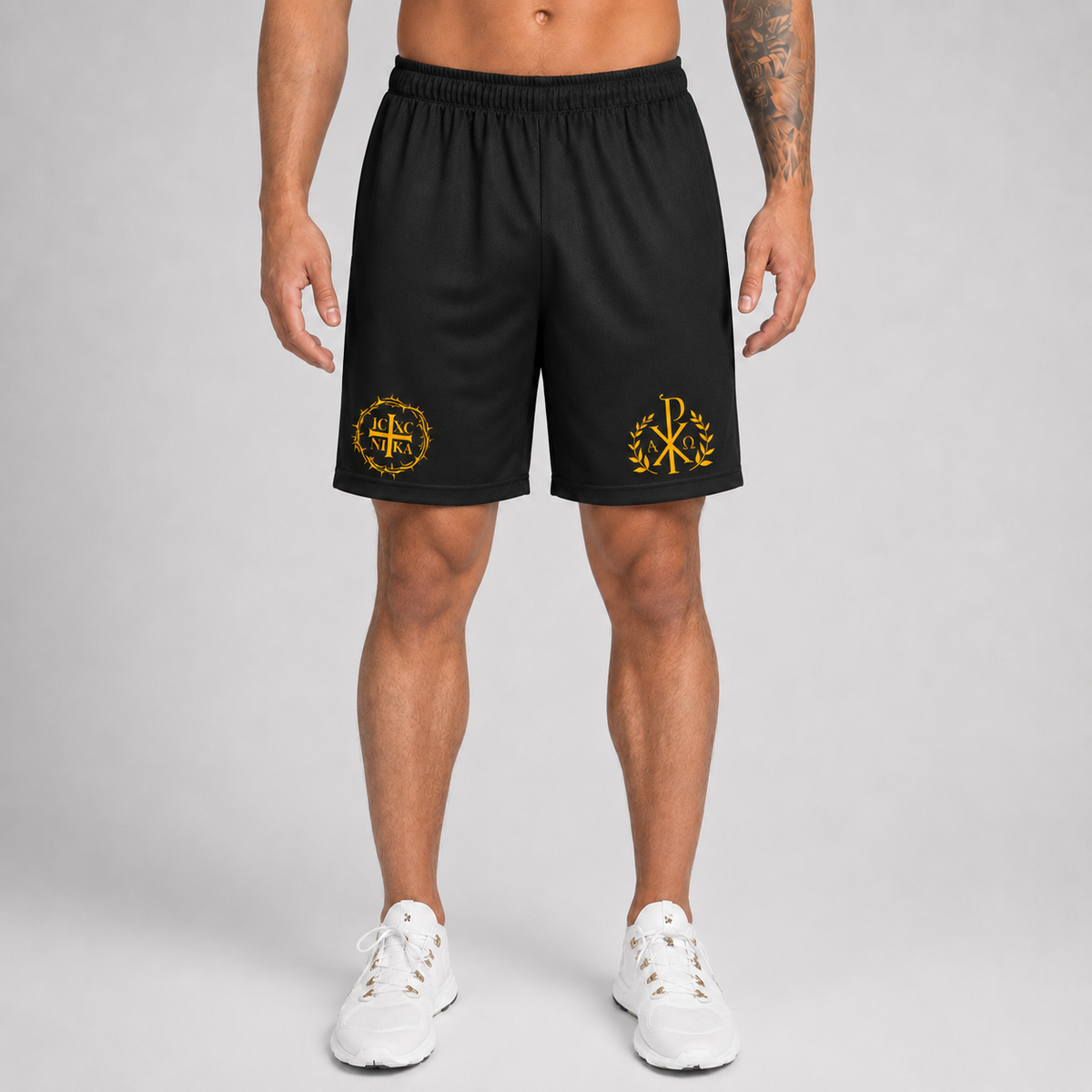 A man modeling black athletic shorts with yellow embroidered logos on the left and right legs, paired with white sneakers, against a light gray studio background.
