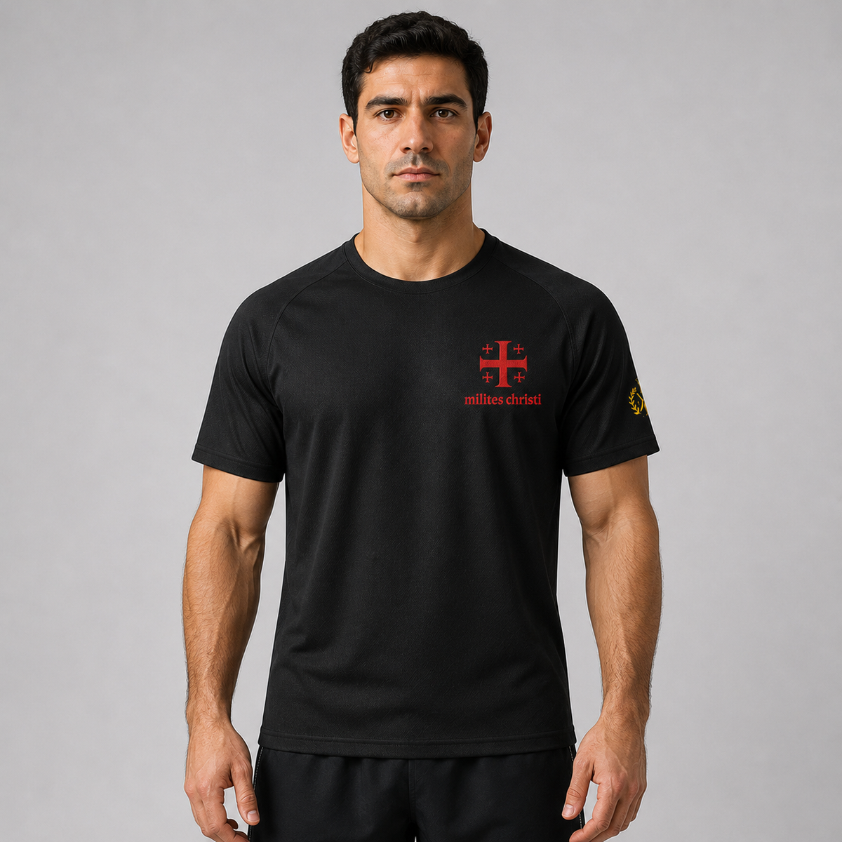 A man wearing a black short-sleeve athletic t-shirt with a red 'milites christi' cross logo on the chest and a yellow sleeve logo, photographed against a neutral gray background.