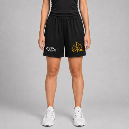 Un model văzut de la talie în jos, purtând pantaloni scurți sport negri cu emblemă albă ιχθυς pe piciorul stâng și monogramă aurie pe cel drept, cu pantofi sport albi, pe un fundal gri de studio.