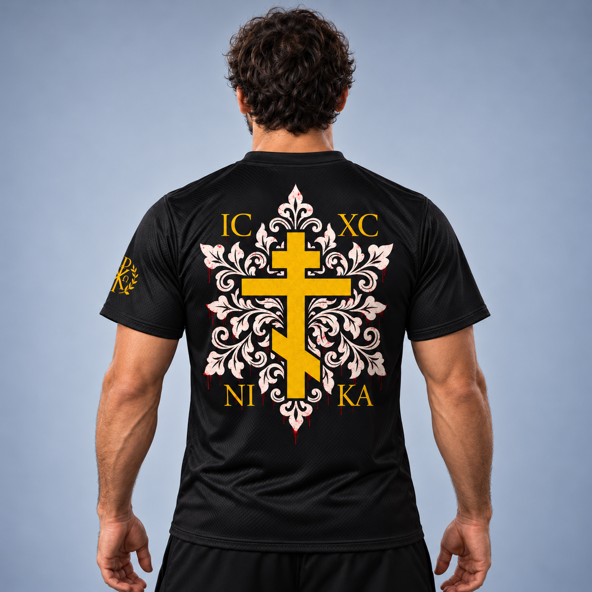 A man wearing a black short-sleeve athletic jersey shown from the back, featuring a large yellow and white ornamental cross graphic with gold letters and a small gold emblem on the sleeve, photographed against a gray gradient studio background.