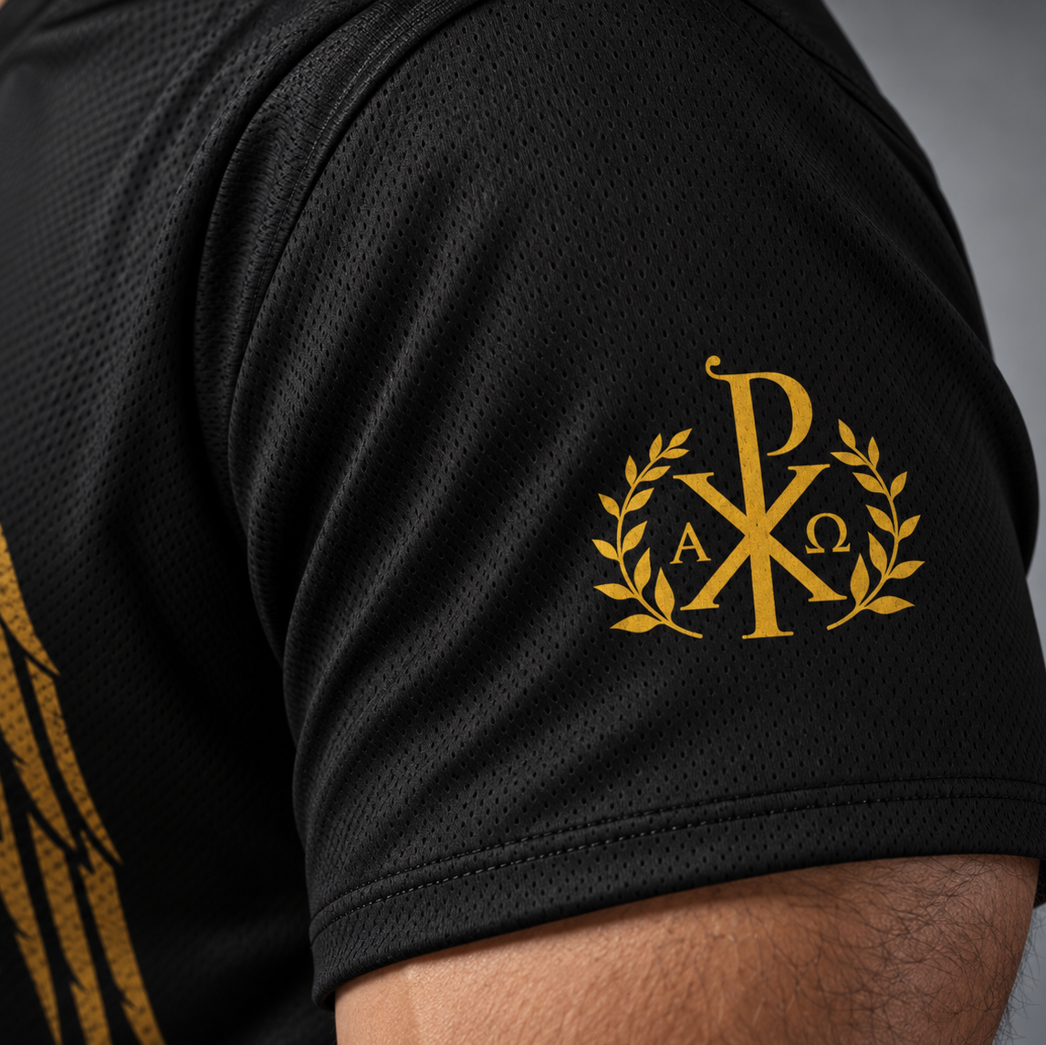 Close-up of a black athletic jersey sleeve featuring a gold monogram crest with laurel branches and a partial gold eagle graphic on the shoulder.