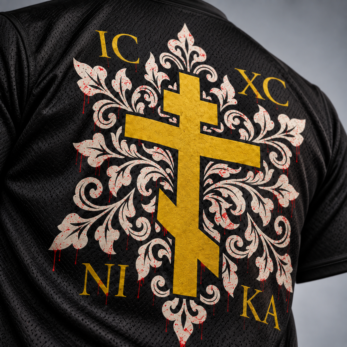 Close-up of the back of a black mesh athletic jersey featuring a large gold cross over an ornate cream damask-style motif with red dripping accents and gold text reading IC XC NI KA.
