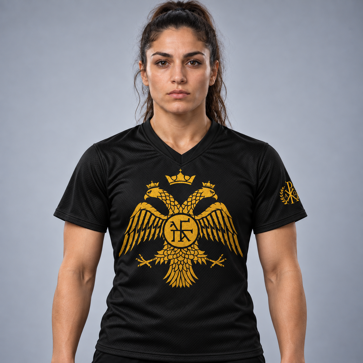 A woman modeling a black short-sleeve athletic jersey with a large gold double-headed eagle crest on the front and a smaller matching crest on the sleeve, photographed against a plain gray studio background.
