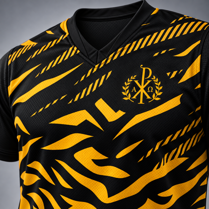 Close-up of a black athletic jersey with a bold yellow abstract pattern and a gold monogram crest on the chest, shown against a neutral gray background.