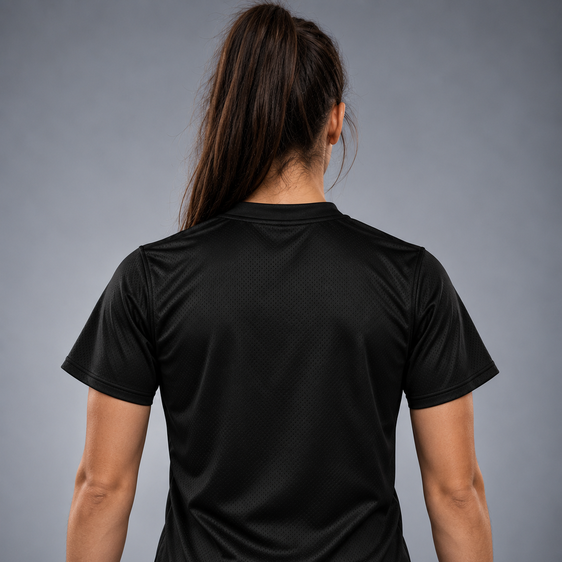 O femeie văzută din spate, purtând un tricou sport negru cu mâneci scurte, care evidențiază textura materialului pe spate, pe un fundal gri neutru de studio.