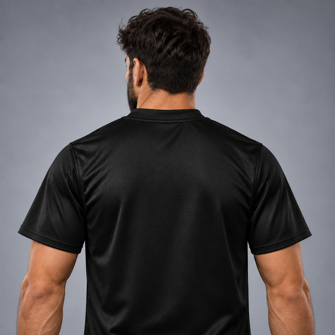 Un bărbat văzut din spate, purtând un tricou sport negru cu mâneci scurte, care evidențiază textura materialului pe spate, pe un fundal gri neutru de studio.