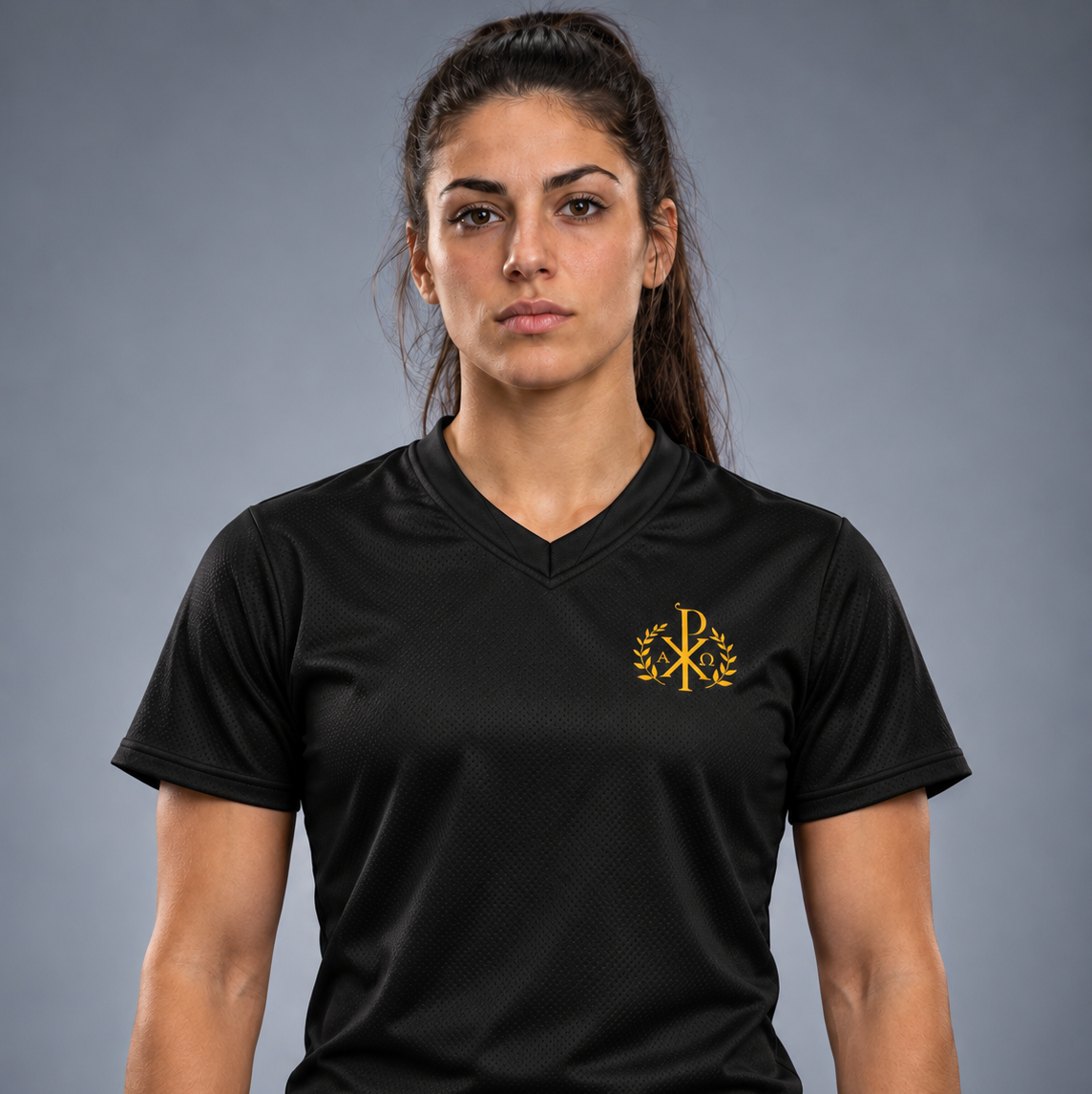 O femeie purtând un tricou sport negru cu mâneci scurte, decolteu în V și emblemă aurie în stânga pieptului, pe un fundal gri uniform de studio.