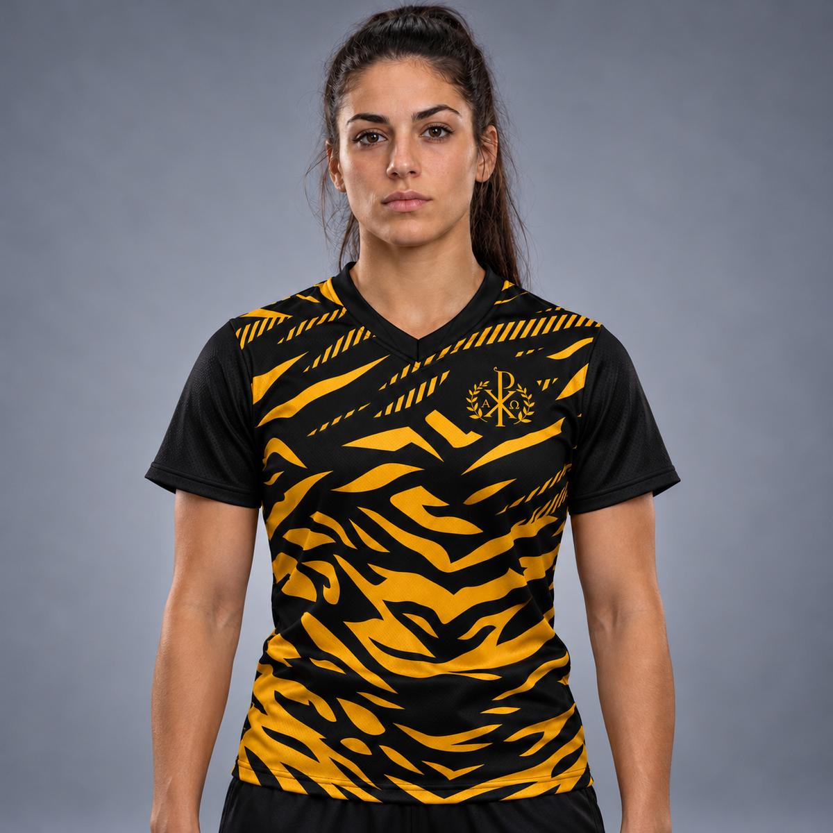 A woman wearing a short-sleeve V-neck athletic jersey with a bold black and yellow tiger-stripe pattern, featuring a gold monogram logo on the chest, displayed on a neutral gray background.