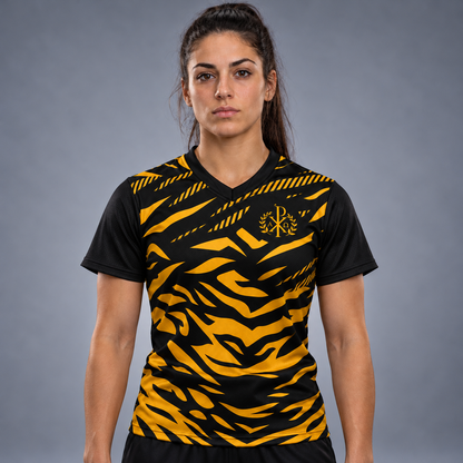 A woman wearing a short-sleeve V-neck athletic jersey with a bold black and yellow tiger-stripe pattern, featuring a gold monogram logo on the chest, displayed on a neutral gray background.