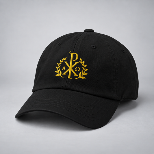 A black baseball cap with a gold embroidered monogram logo on the front, photographed on a neutral gray background.