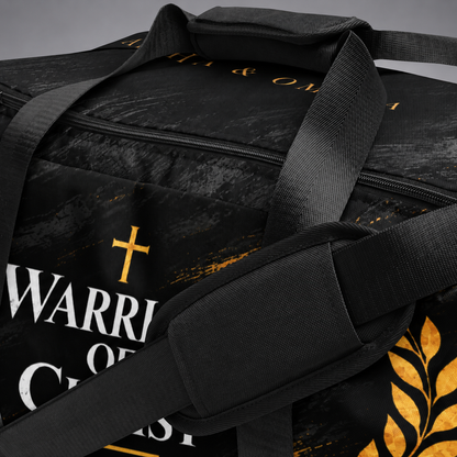 A close-up of a black duffel bag with a distressed texture, featuring a gold cross, white and gold text reading 'WARRIOR OF CHRIST', and a gold laurel leaf design.