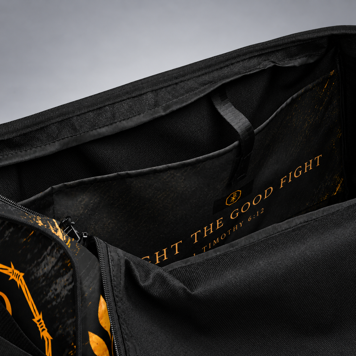 Close-up of the interior of a black bag or duffel with gold printed text reading 'FIGHT THE GOOD FIGHT' and a small circular logo, plus gold graphic accents along a zipper.