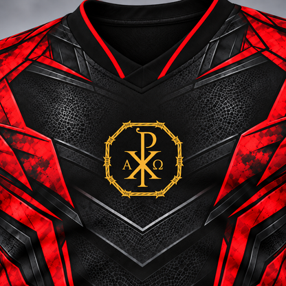 Close-up of a black and red soccer jersey with a gold Chi-Rho monogram on the chest, featuring a textured leather-like pattern and geometric shoulder panels.