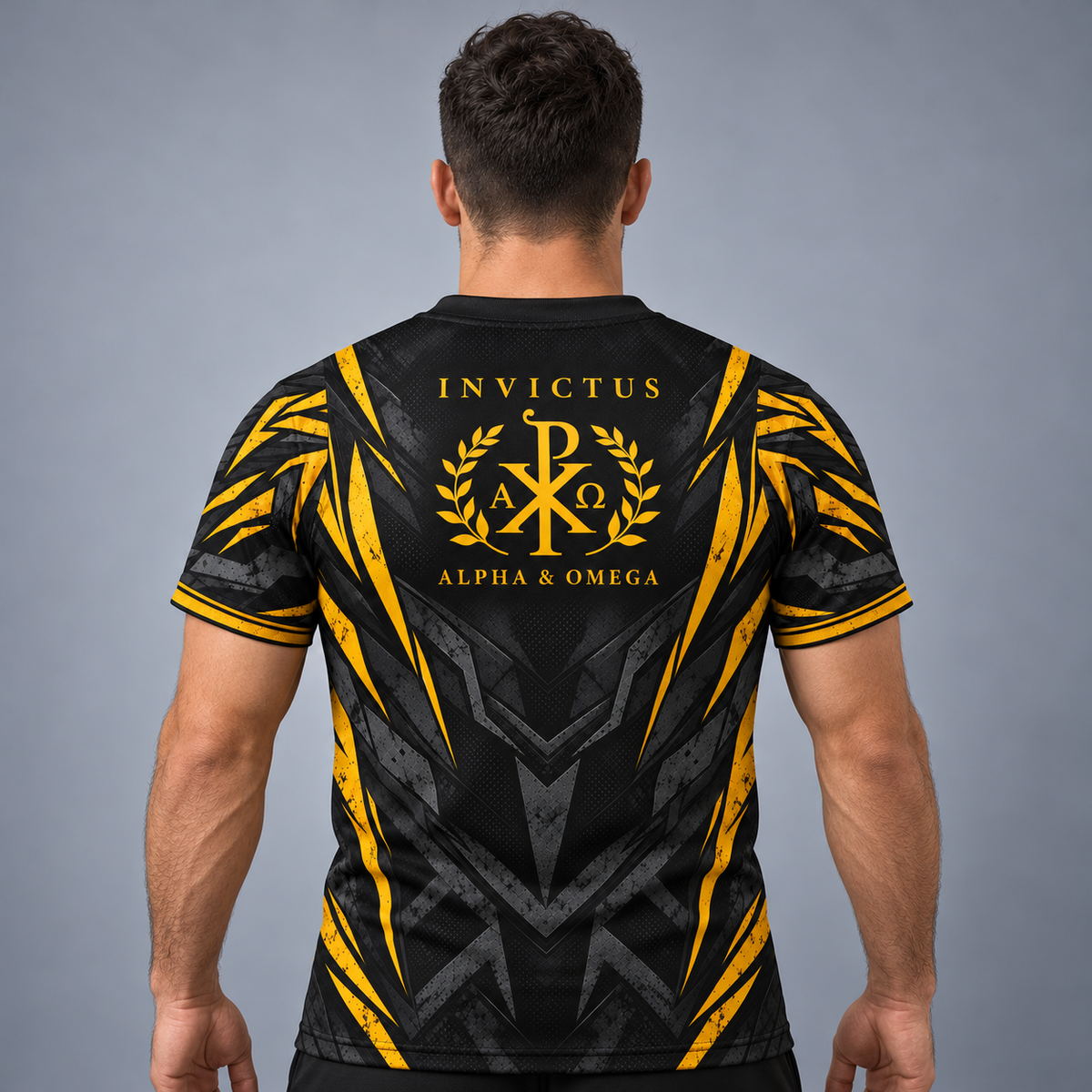 A man viewed from behind wearing a black athletic jersey with a large gold and gray graphic on the back reading 'INVICTUS ALPHA & OMEGA' with a monogram emblem.
