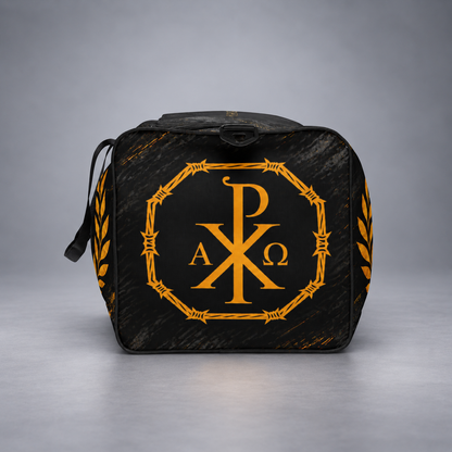 A black bag with a distressed wood-grain texture, featuring a prominent golden-yellow Chi Rho monogram inside an octagonal frame on the front, with laurel leaf details on the sides.
