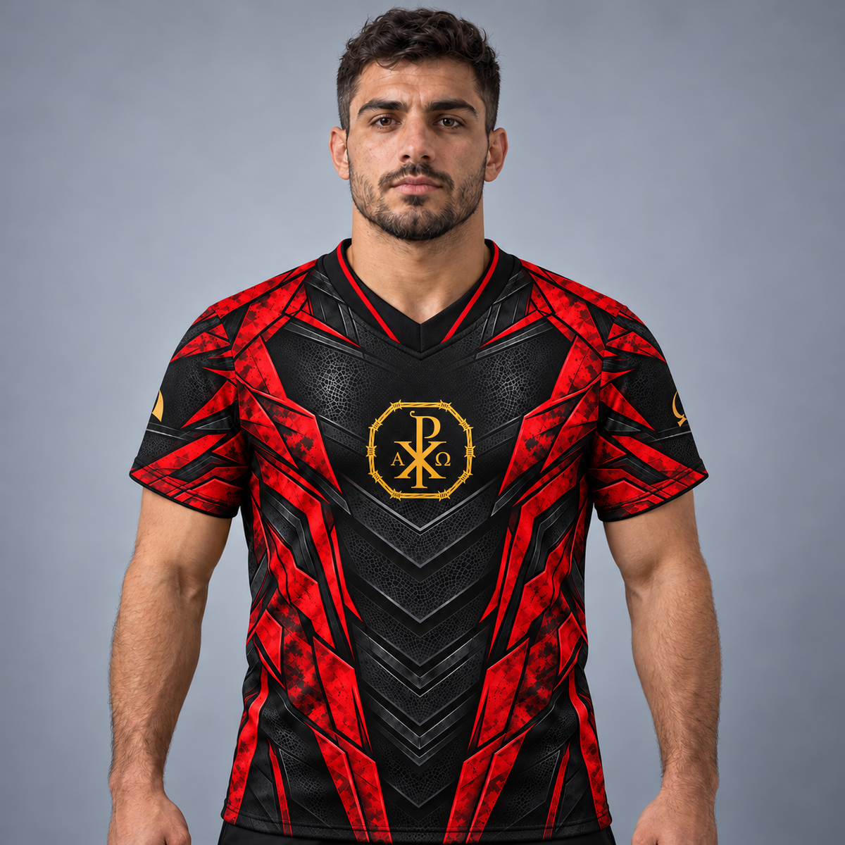 A man modeling a black and red athletic jersey with a gold Chi-Rho emblem on the chest, set against a solid gray studio background.