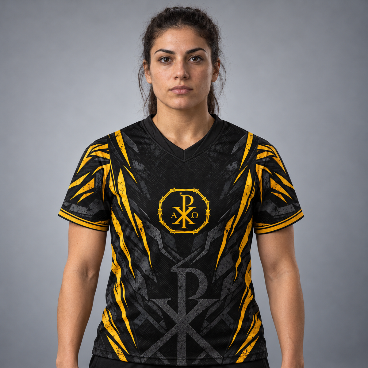 A woman modeling a black and yellow athletic jersey with a V-neck and a central monogram logo, photographed against a neutral gray studio background.