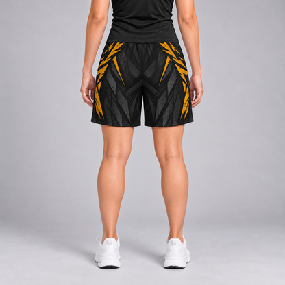 A person shown from the back wearing black athletic shorts with a bold yellow geometric pattern, a black athletic top, and white sneakers against a light gray studio background.