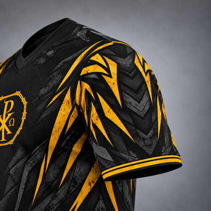 Close-up of a black athletic jersey with a bold yellow and gray geometric pattern, featuring a yellow crest on the chest and a striped collar, set against a neutral gray background.