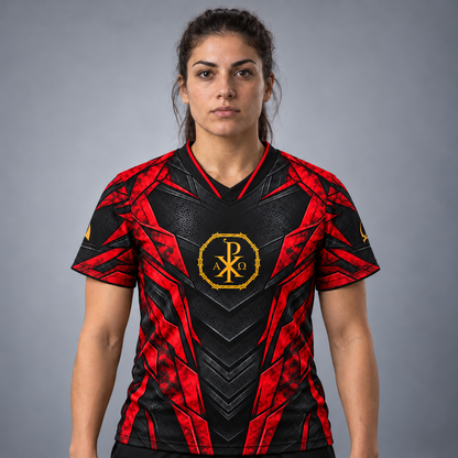 A woman modeling a short-sleeve athletic jersey with a black and red geometric pattern and a gold Chi-Rho emblem on the chest, set against a neutral gray studio background.