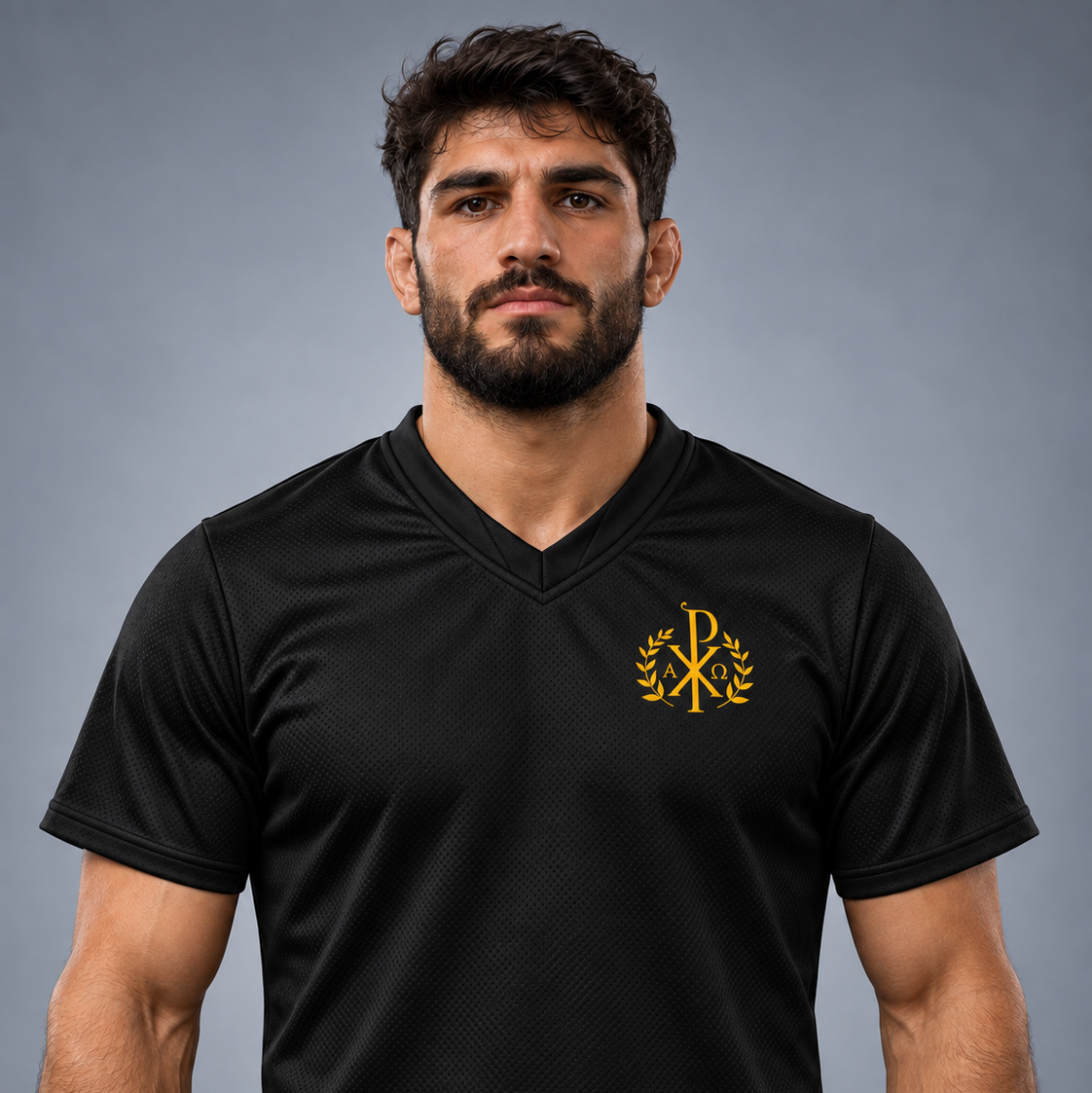 Un bărbat purtând un tricou sport negru cu decolteu în V și monogramă aurie în stânga pieptului, pe un fundal gri uniform de studio.
