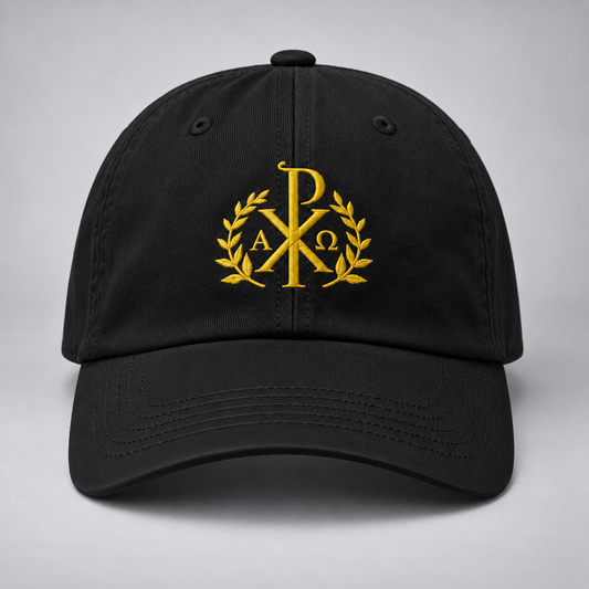A black baseball cap with a gold embroidered Chi Rho monogram wreath on the front, set against a neutral gray background.