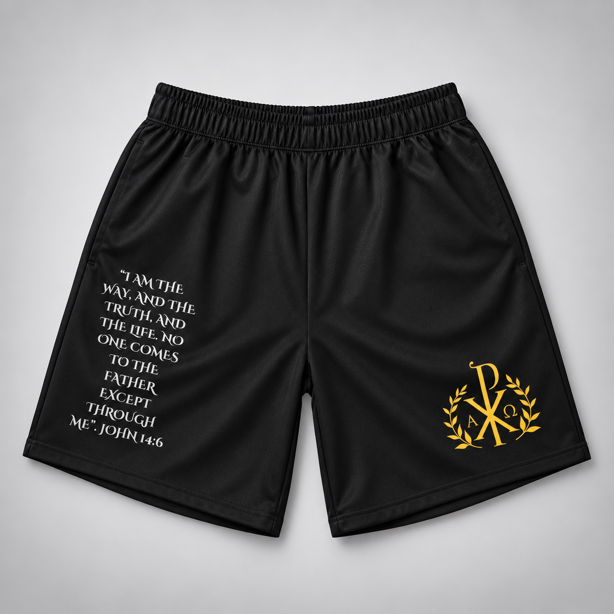 Black athletic shorts with a white biblical quote printed on the left leg and a gold Chi-Rho monogram with laurel leaves on the right leg, displayed on a neutral gray background.