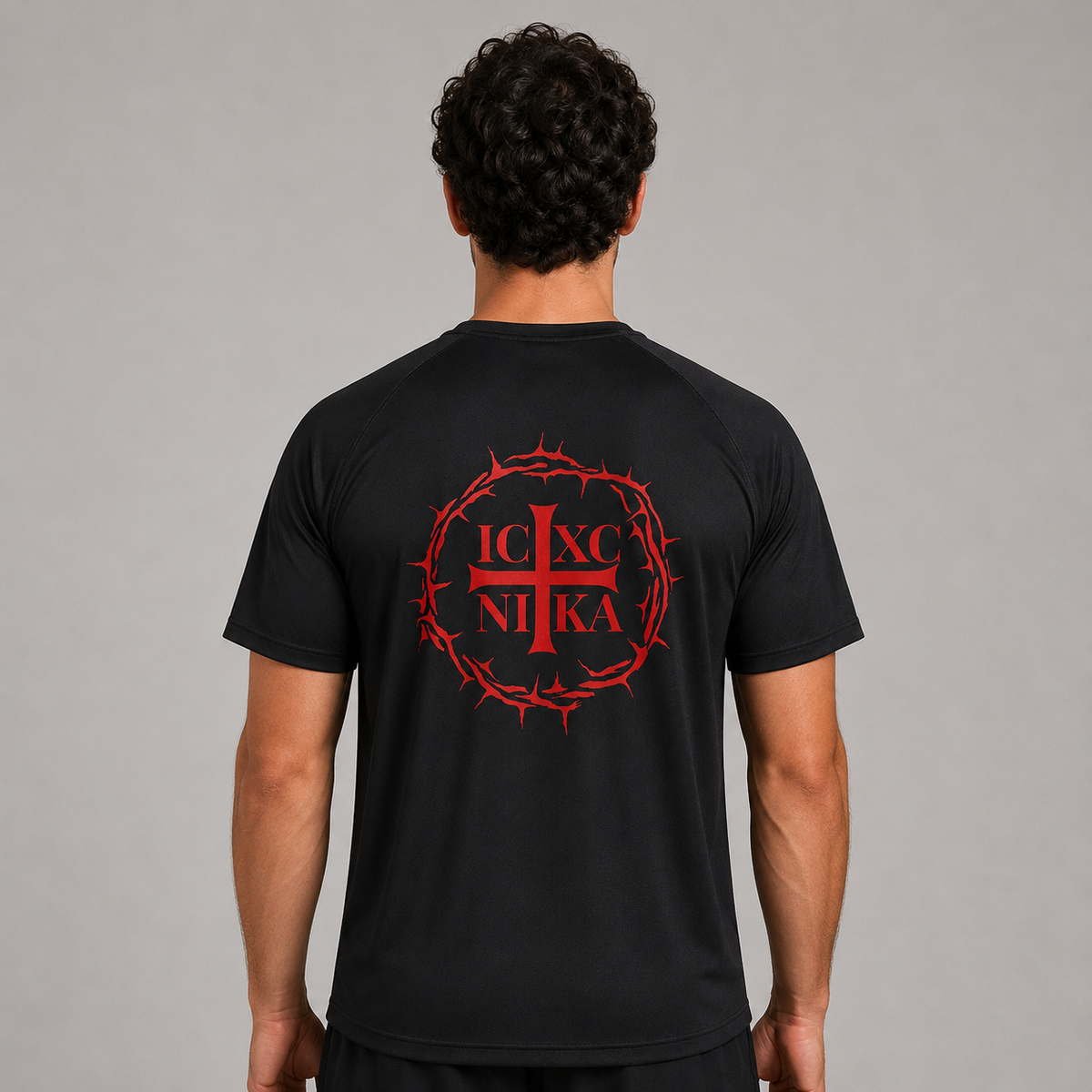 Un bărbat văzut din spate, purtând un tricou sport negru cu un imprimeu roșu. Imprimeul reprezintă o cruce roșie într-o cunună de spini, cu literele grecești „IC XC NI KA” integrate în model