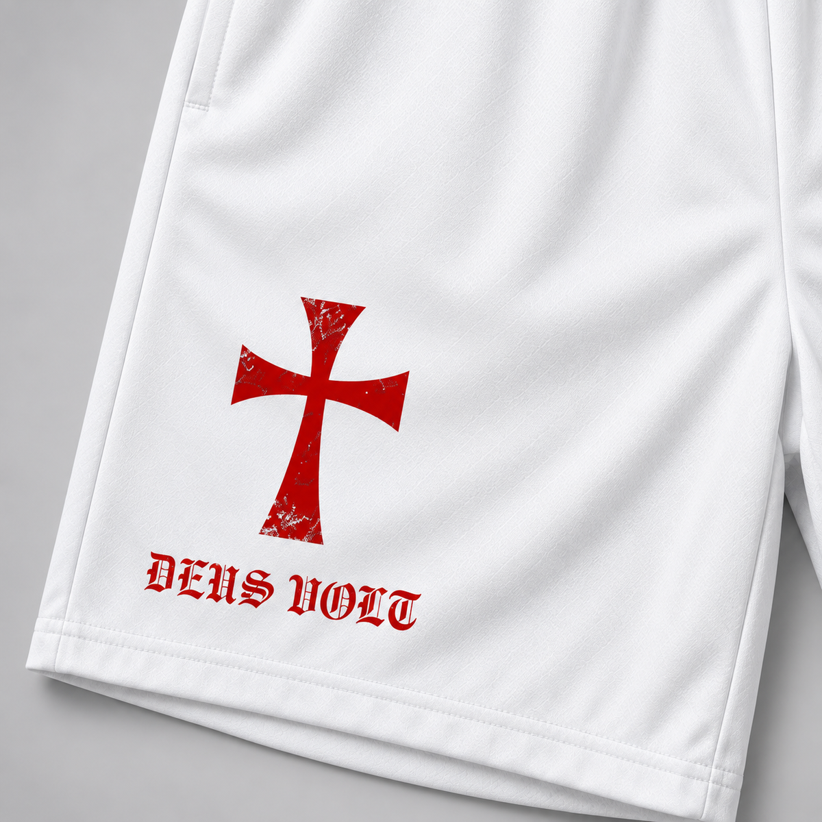 White athletic shorts featuring a distressed red cross graphic and the text 'DEUS VULT' in red Gothic lettering on the left leg, shown against a neutral gray background.