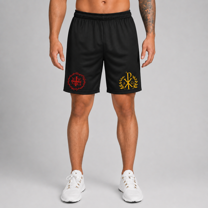 A man modeling black athletic shorts with red and yellow embroidered logos, paired with white sneakers, against a neutral gray studio background.